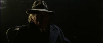Movie still from “The Keep” (1983), directed by Michael Mann – An old man wearing a hat in the dark; Close Up shot, Over the shoulder angle