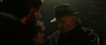 Movie still from “The Keep” (1983), directed by Michael Mann – An older man wearing a hat talking to a young woman; Close Up shot, Over the shoulder angle