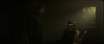 Movie still from “The Keep” (1983), directed by Michael Mann – A man in a hat and a man with a beard; Medium shot, Over the shoulder angle