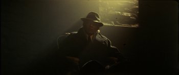 Movie still from “The Keep” (1983), directed by Michael Mann – A man wearing a hat sitting in a chair; Medium shot, Low angle