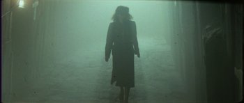 Movie still from “The Keep” (1983), directed by Michael Mann – A woman walking in the middle of a foggy street; Wide shot, Over the shoulder angle