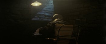 Movie still from “The Keep” (1983), directed by Michael Mann – An old man sitting in a chair in a dark room; Medium shot, Over the shoulder angle