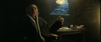 Movie still from “The Keep” (1983), directed by Michael Mann – An old man sitting at a table in a dark room; Medium shot, Low angle