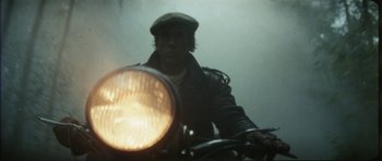 Movie still from “The Keep” (1983), directed by Michael Mann – A man riding on the back of a motorcycle; Close Up shot, Low angle