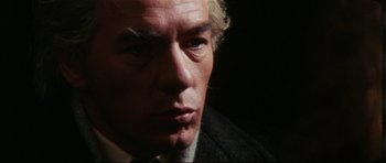 Movie still from “The Keep” (1983), directed by Michael Mann – An older man wearing a suit and tie looking at the camera; Close Up shot, Over the shoulder angle