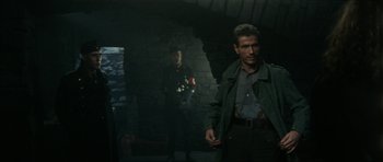 Movie still from “The Keep” (1983), directed by Michael Mann – A man standing next to another man holding a gun; Medium shot, Over the shoulder angle