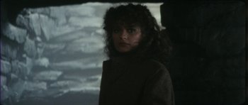 Movie still from “The Keep” (1983), directed by Michael Mann – A woman in a brown jacket standing in front of a body of water; Close Up shot, Over the shoulder angle