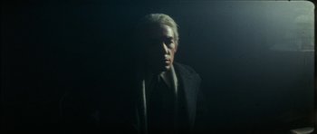 Movie still from “The Keep” (1983), directed by Michael Mann – A man in a suit and tie in a dark room; Medium shot, Low angle