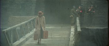 Movie still from “The Keep” (1983), directed by Michael Mann – A woman in a trench coat carrying a suitcase; Wide shot, High angle