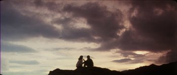 Movie still from “The Keep” (1983), directed by Michael Mann – Two people sitting on top of a hill under a cloudy sky; Wide shot, Low angle