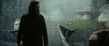 Movie still from “The Keep” (1983), directed by Michael Mann – A man with a long beard walking down a bridge; Wide shot, Low angle