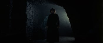 Movie still from “The Keep” (1983), directed by Michael Mann – A man standing in the dark in front of a stone wall; Wide shot, Low angle