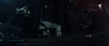 Movie still from “The Keep” (1983), directed by Michael Mann – A small house in the middle of a dark forest; Extreme Wide shot, Low angle