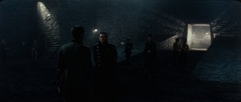 Movie still from “The Keep” (1983), directed by Michael Mann – A group of men standing in a dark room; Wide shot, Over the shoulder angle