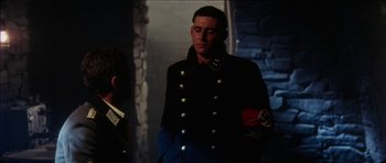 Movie still from “The Keep” (1983), directed by Michael Mann – A man in a military uniform standing next to another man; Medium shot, Over the shoulder angle