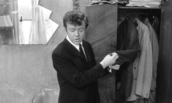 Movie still from “The Knack... and How to Get It” (1965), directed by Richard Lester – A man in a suit and tie holding a suit jacket; Medium shot, Over the shoulder angle