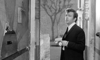 Movie still from “The Knack... and How to Get It” (1965), directed by Richard Lester – A black and white photo of a man standing in front of a door; Medium shot, Low angle