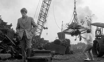 Movie still from “The Knack... and How to Get It” (1965), directed by Richard Lester – A black and white photo of a man standing in front of a crane; Wide shot, Low angle