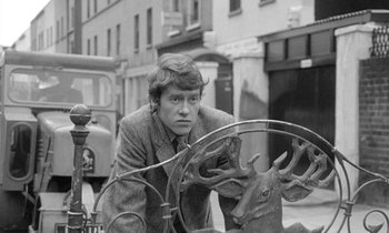 Movie still from “The Knack... and How to Get It” (1965), directed by Richard Lester – A man leaning against a metal sculpture of a deer; Medium shot, Low angle