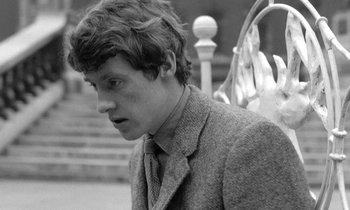 Movie still from “The Knack... and How to Get It” (1965), directed by Richard Lester – A man in a suit and tie standing next to a railing; Close Up shot, Low angle