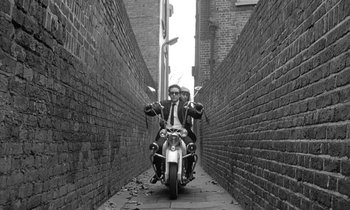 Movie still from “The Knack... and How to Get It” (1965), directed by Richard Lester – A man riding a motorcycle down the middle of an alleyway; Wide shot, Low angle