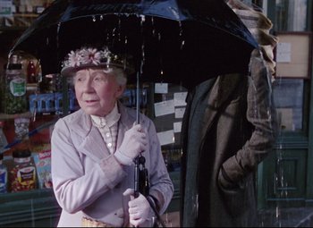 Movie still from “The Ladykillers” (1955), directed by Alexander Mackendrick – An older woman holding an umbrella while standing next to a man; Medium shot, Over the shoulder angle