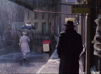 Movie still from “The Ladykillers” (1955), directed by Alexander Mackendrick – A man and a woman walking down a street in the pouring rain; Wide shot, Over the shoulder angle