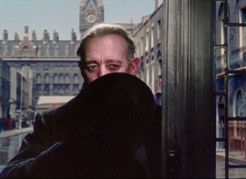 Movie still from “The Ladykillers” (1955), directed by Alexander Mackendrick – A man hiding his face behind a black cloth; Medium shot, Over the shoulder angle