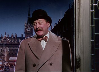 Movie still from “The Ladykillers” (1955), directed by Alexander Mackendrick – A man in a hat and a suit standing in front of a building; Medium shot, Low angle