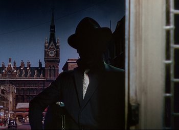 Movie still from “The Ladykillers” (1955), directed by Alexander Mackendrick – A man in a suit and hat standing in front of a building; Wide shot, Low angle