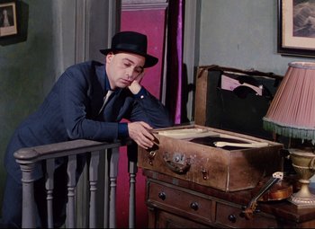 Movie still from “The Ladykillers” (1955), directed by Alexander Mackendrick – A man in a hat and a suit jacket leaning on a suitcase; Medium shot, High angle