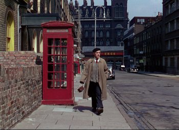 Movie still from “The Ladykillers” (1955), directed by Alexander Mackendrick – A man walking down the street in front of a red telephone booth; Wide shot, Low angle