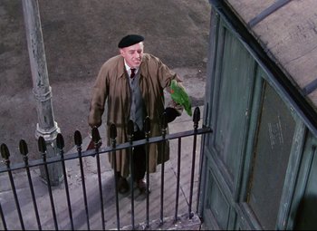 Movie still from “The Ladykillers” (1955), directed by Alexander Mackendrick – An old man wearing a coat and hat is standing on the steps of a building; Medium shot, Overhead angle