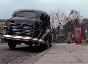 Movie still from “The Ladykillers” (1955), directed by Alexander Mackendrick – An old car parked on the side of the street; Wide shot, High angle