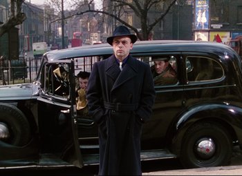 Movie still from “The Ladykillers” (1955), directed by Alexander Mackendrick – A man standing in front of an old fashioned car; Medium shot, Low angle