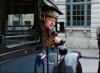 Movie still from “The Ladykillers” (1955), directed by Alexander Mackendrick – A man in a hat is sitting in the driver's seat of an old car; Medium shot, Low angle