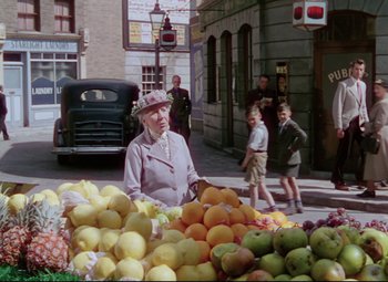 Movie still from “The Ladykillers” (1955), directed by Alexander Mackendrick – An older woman standing in front of a fruit stand; Wide shot, High angle