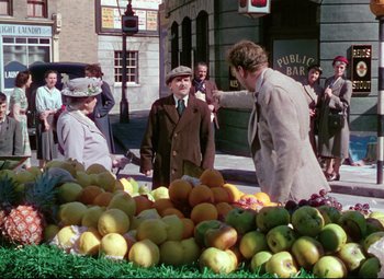 Movie still from “The Ladykillers” (1955), directed by Alexander Mackendrick – A group of people standing next to a pile of fruit; Wide shot, Over the shoulder angle