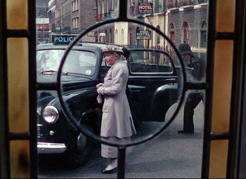 Movie still from “The Ladykillers” (1955), directed by Alexander Mackendrick – An older woman is standing in front of an old black car; Wide shot, Over the shoulder angle