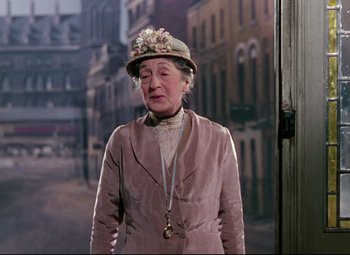 Movie still from “The Ladykillers” (1955), directed by Alexander Mackendrick – An older woman wearing a hat standing in front of buildings; Medium shot, Low angle