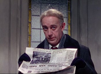 Movie still from “The Ladykillers” (1955), directed by Alexander Mackendrick – A man holding a newspaper while wearing gloves and a tie; Close Up shot, Low angle