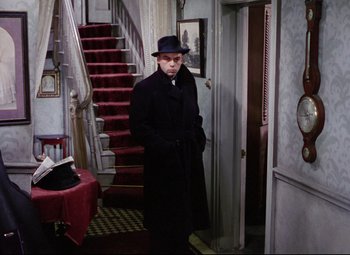 Movie still from “The Ladykillers” (1955), directed by Alexander Mackendrick – A man standing in front of a staircase wearing a hat; Wide shot, High angle