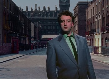 Movie still from “The Ladykillers” (1955), directed by Alexander Mackendrick – A man wearing a suit and tie standing in a street; Medium shot, Low angle