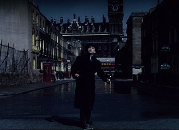 Movie still from “The Ladykillers” (1955), directed by Alexander Mackendrick – A man standing on the side of the street in the dark; Wide shot, Low angle