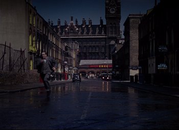 Movie still from “The Ladykillers” (1955), directed by Alexander Mackendrick – A man in a suit and tie running down a street; Extreme Wide shot, High angle