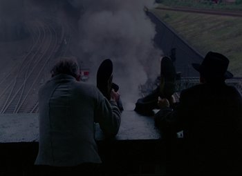 Movie still from “The Ladykillers” (1955), directed by Alexander Mackendrick – A group of people sitting next to each other on a platform; Wide shot, High angle