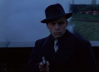 Movie still from “The Ladykillers” (1955), directed by Alexander Mackendrick – A man in a suit and hat holding a cell phone; Medium shot, Low angle