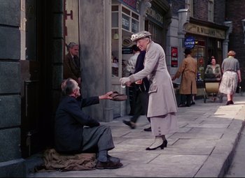 Movie still from “The Ladykillers” (1955), directed by Alexander Mackendrick – An old woman handing a shoe to a man sitting on the sidewalk; Wide shot, High angle