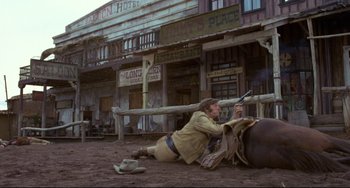 Movie still from “The Last Movie” (1971), directed by Dennis Hopper – A man laying on the ground in front of a building; Wide shot, Low angle