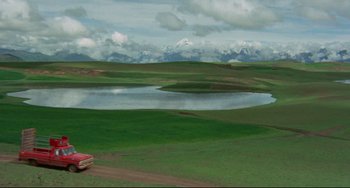 Movie still from “The Last Movie” (1971), directed by Dennis Hopper – A green field with a lake and mountains in the background; Extreme Wide shot, High angle